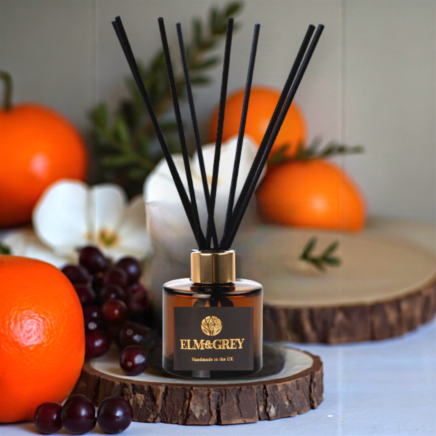 Diffuser with black sticks on a wooden coaster surrounded by fruits and flowers
