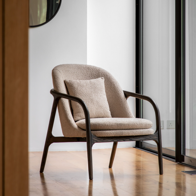 A taupe upholstered armchair with a dark wood frame and plush cushions, positioned in a modern interior setting.