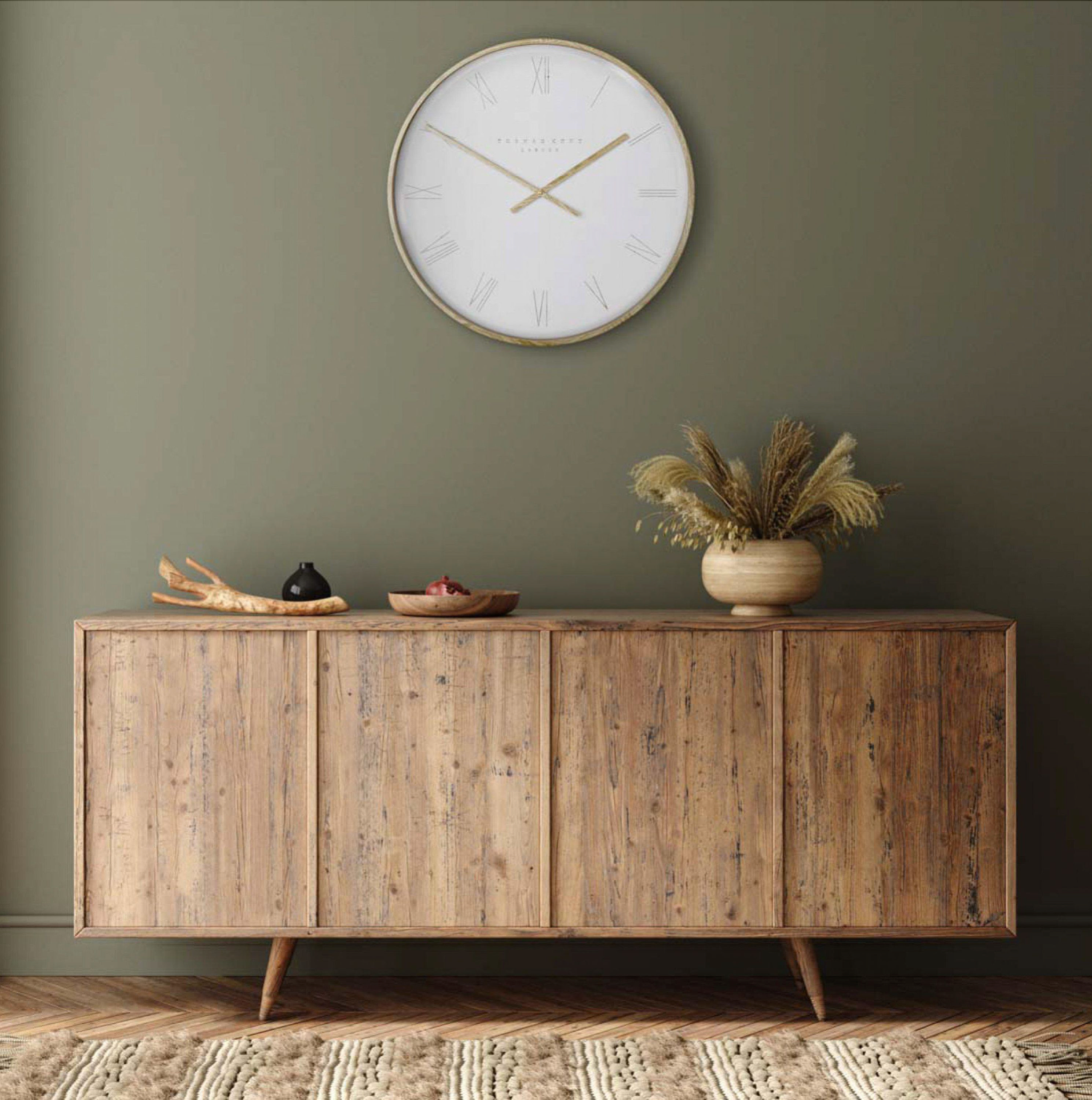 Wooden sideboard with decorative items against a green wall with a clock.