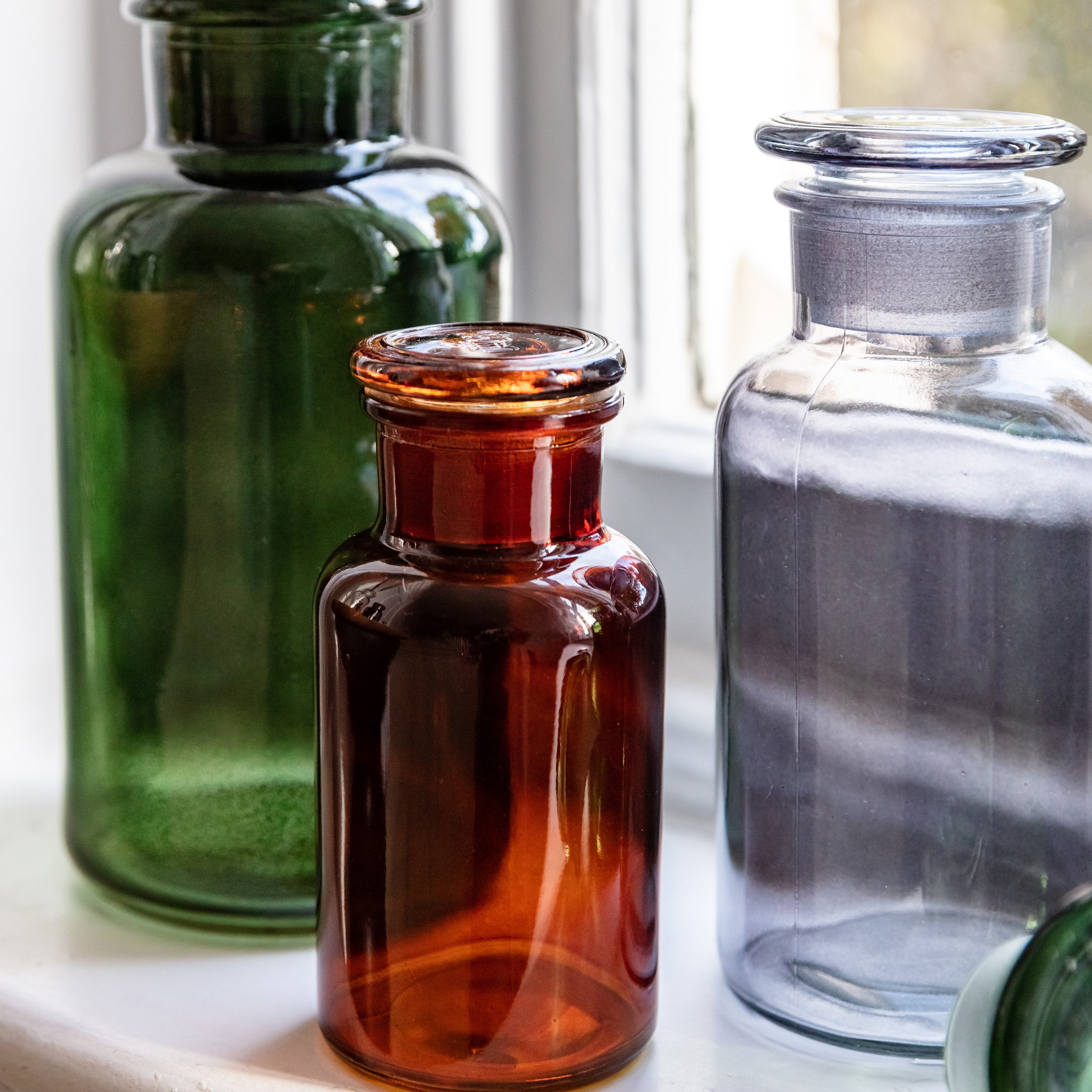 Trio of smoky grey, green and amber apothecary style bottles on a window ledge