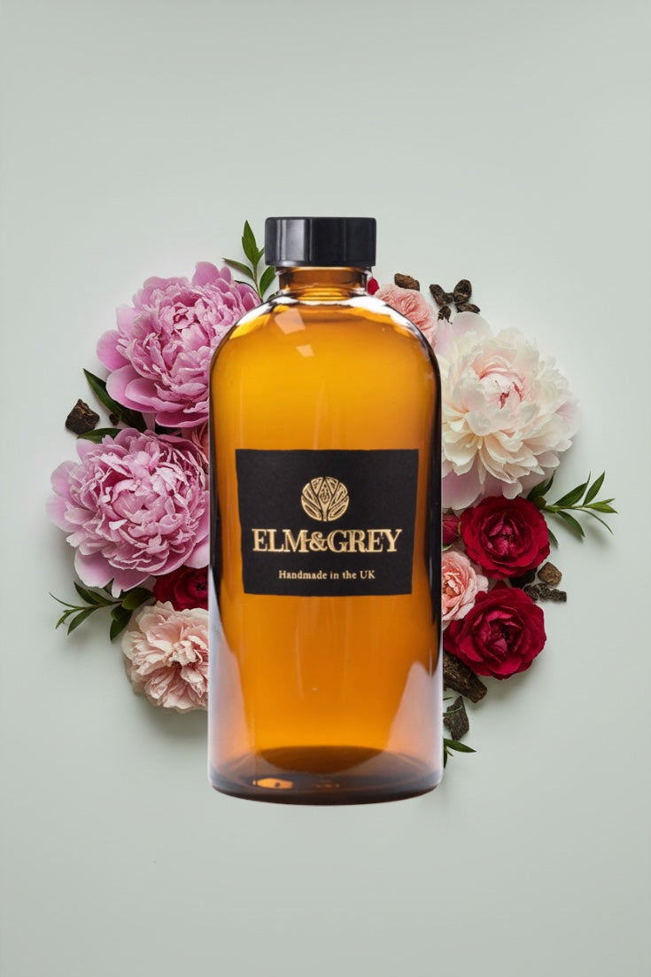 Bottle of Elm & Grey diffuser refill liquid  surrounded by flowers on a light background