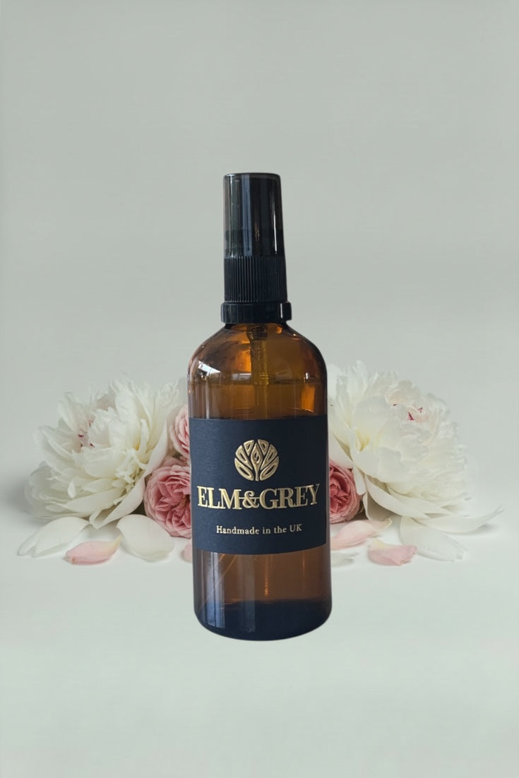 Amber glass bottle with black cap and 'Elm & Grey' label on a light background with flowers.