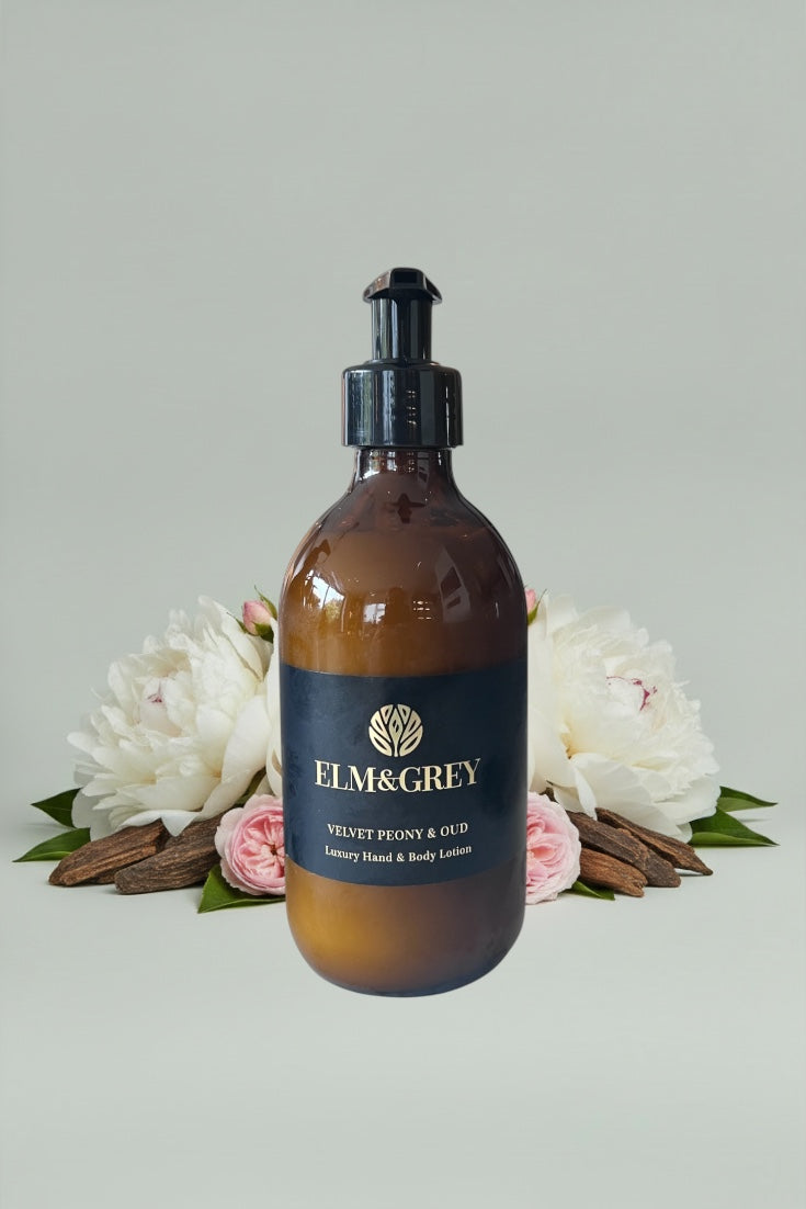 Amber glass bottle with black cap labeled 'Elm&Grey' on a light grey background with flowers and cinnamon sticks.