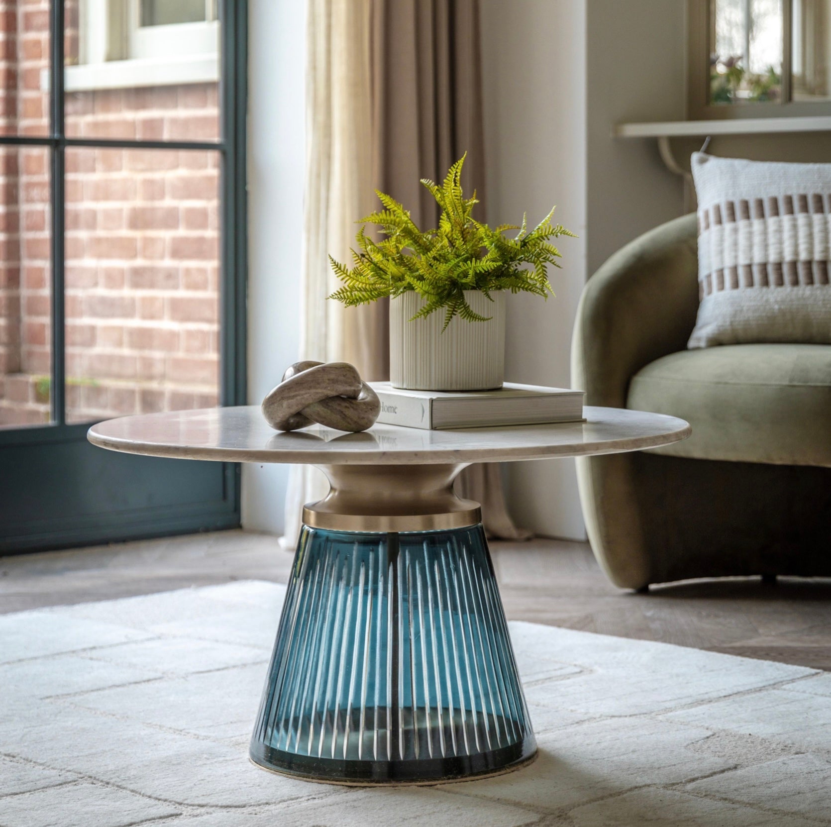 Round marble coffee table with a glass base in a living room setting
