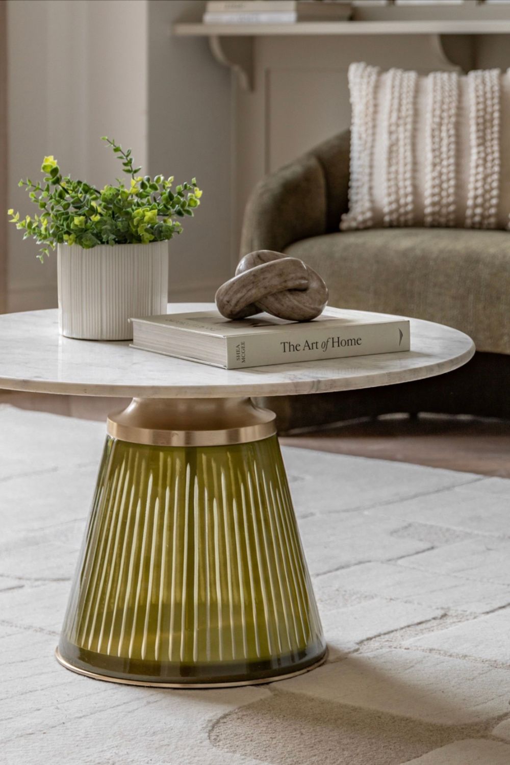 Decorative side table with green glass base and white marble  top in a living room setting.