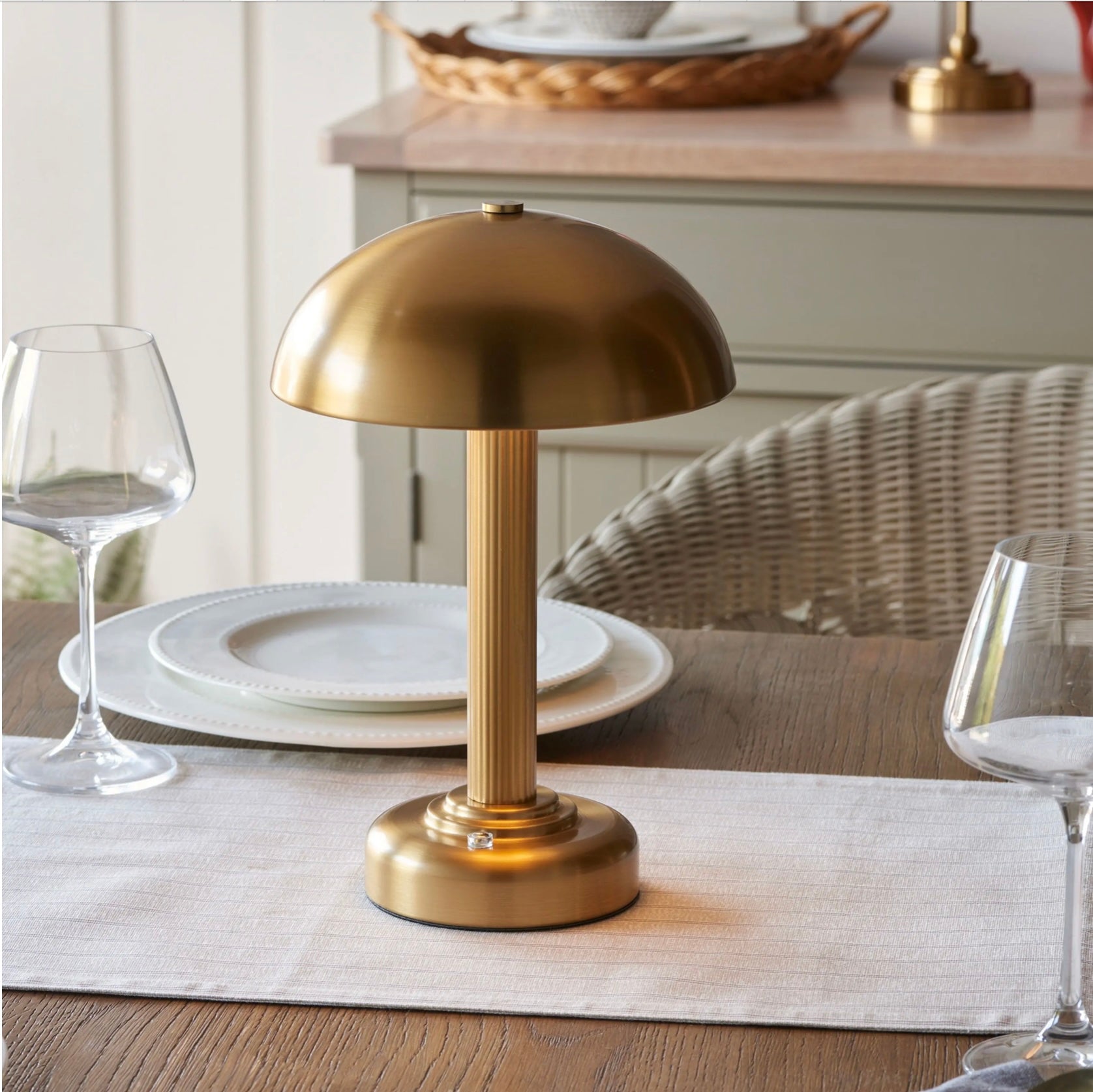 Warm brass able lamp on a dining table with plates and glasses in the background
