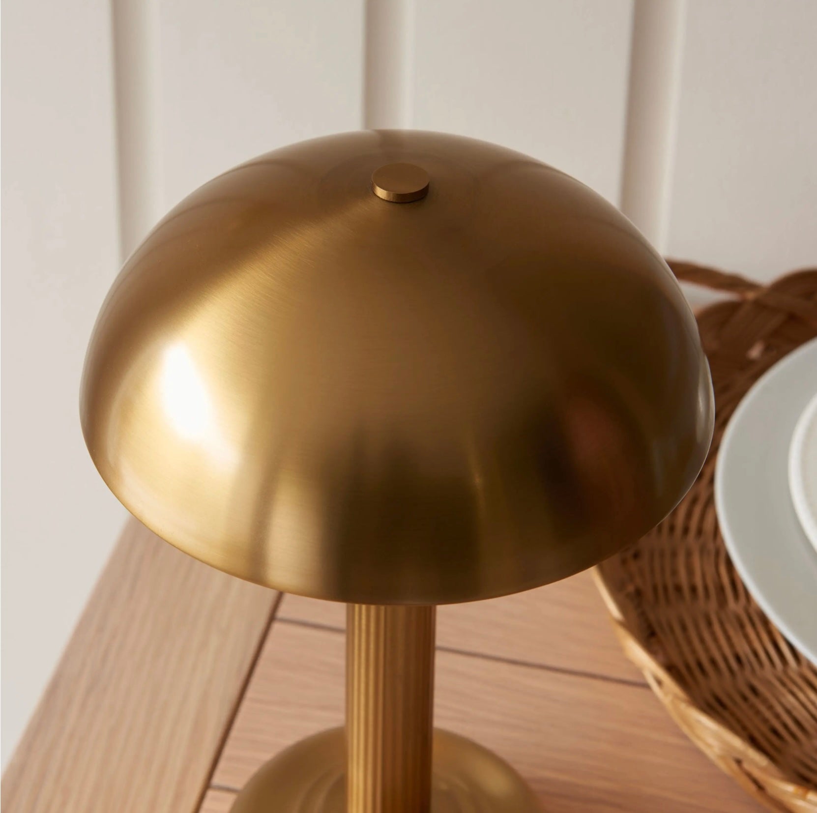Warm brass table lamp on a wooden surface with a wicker basket in the background