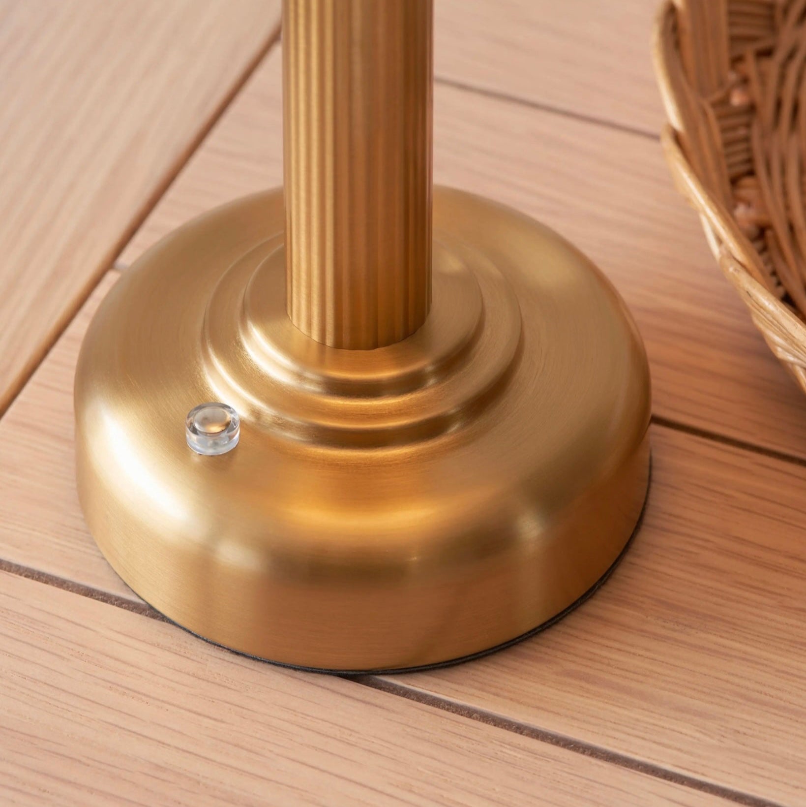 Brass-coluored base on a wooden surface with a wicker basket in the background