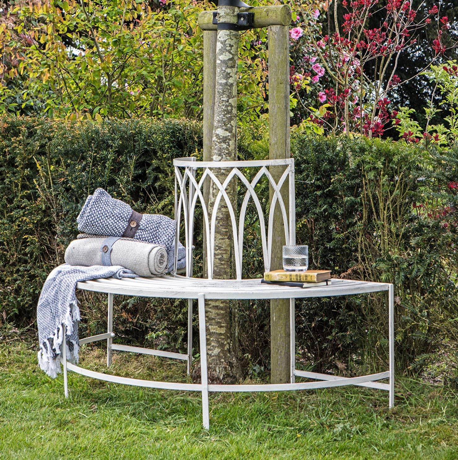 White metal bench with folded towels and a glass of water in a garden setting