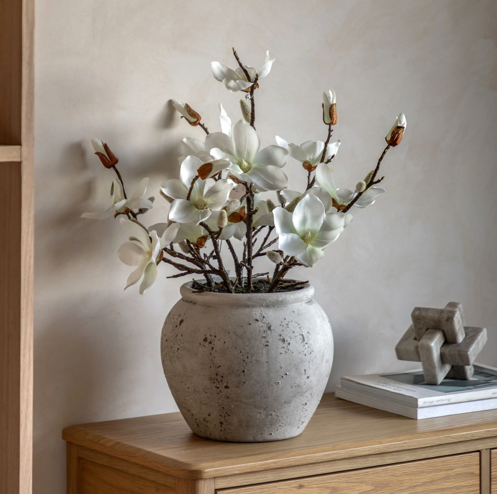 White flowers in a textured vase on a wooden surface with a neutral background