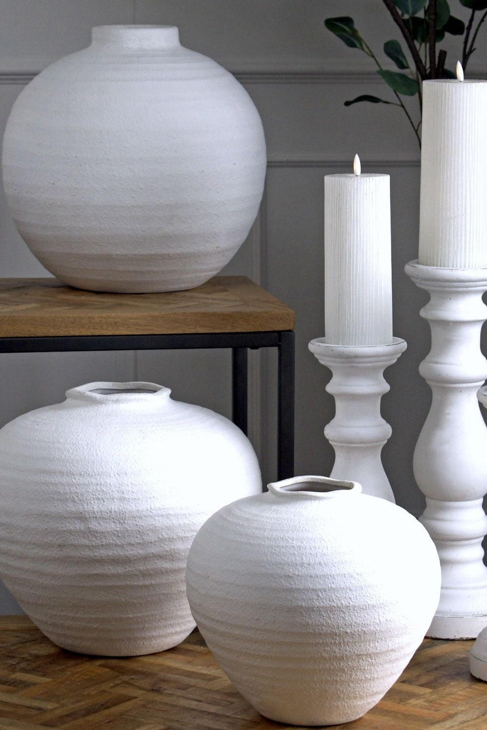White ceramic vases and candle holders on a wooden surface with a neutral background