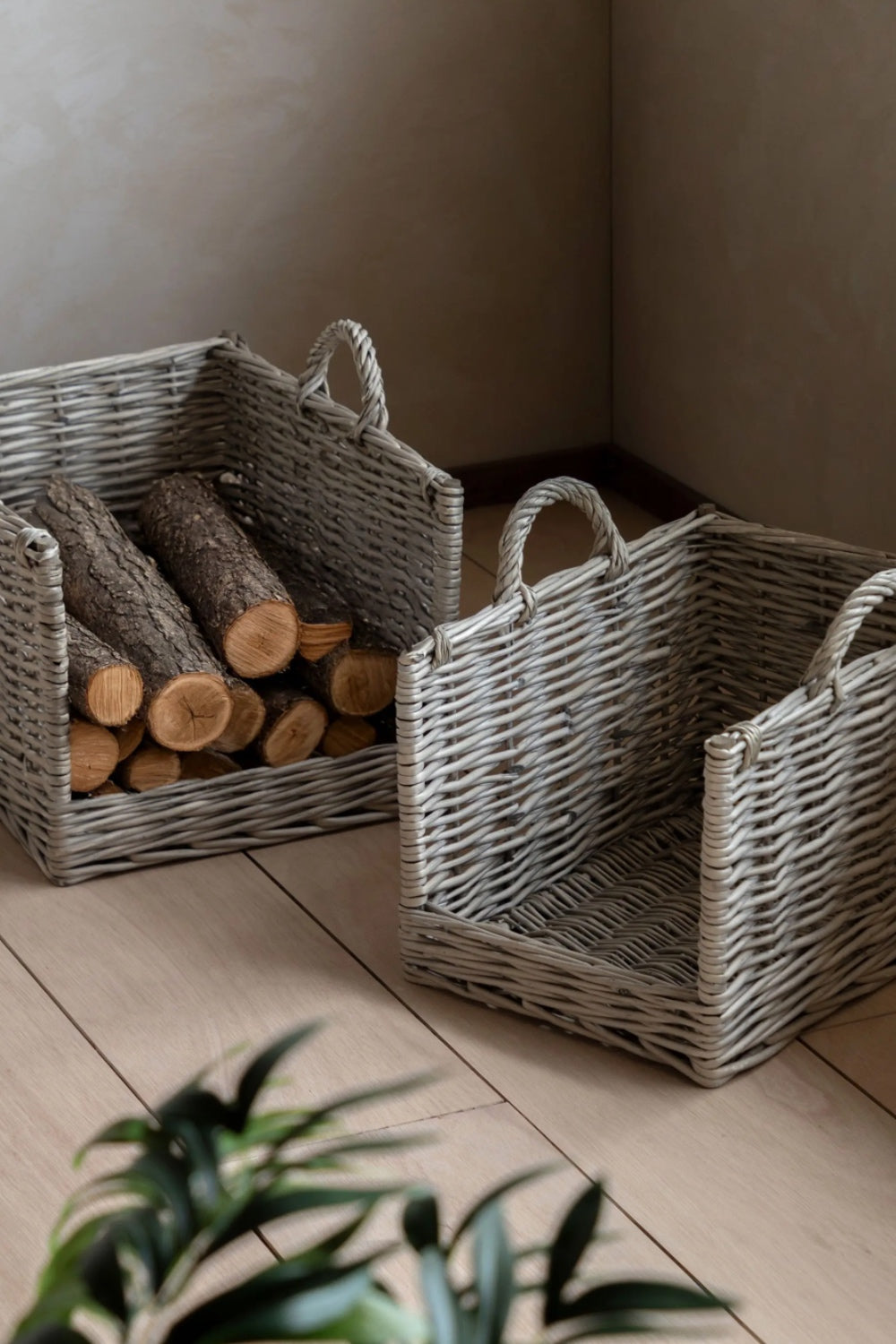 Two wicker baskets with handles on a wooden floor, one containing logs.