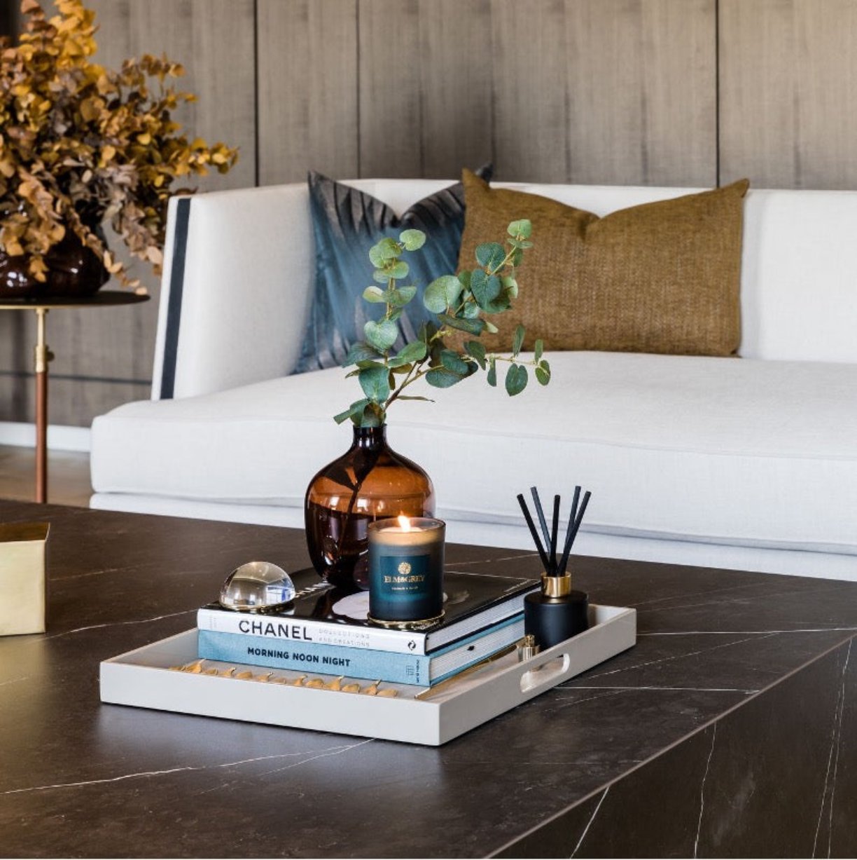 Square tray in latte from mojoo with a pile of books and black rred diffuser and blue candle and amber vase with eucalyptus